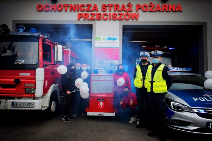Strażacy, policjanci i przedstawiciele fundacji przy nakrętkowym wozie strażackim w Przeciszowie